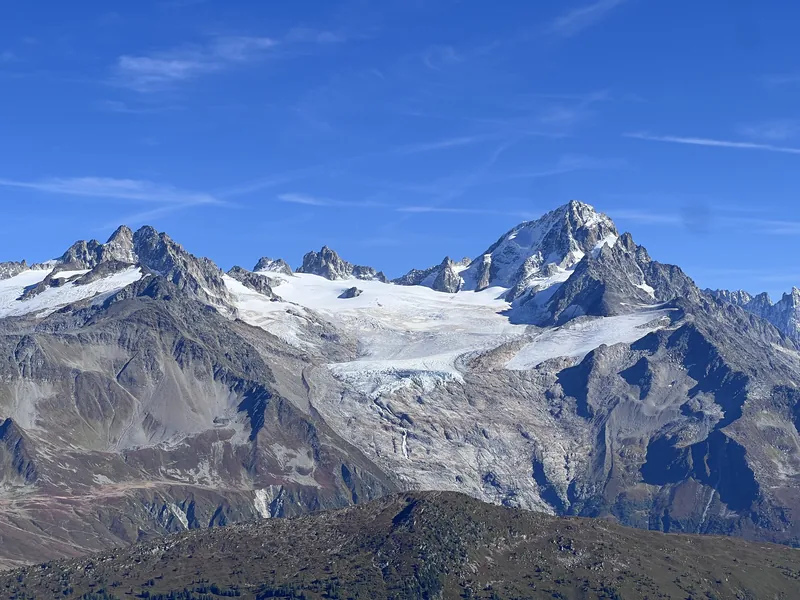 Ein Gletscher zieht sich zwischen schneebedeckten Granitgipfeln des Mont-Blanc-Massivs unter klarem blauem Himmel herab.