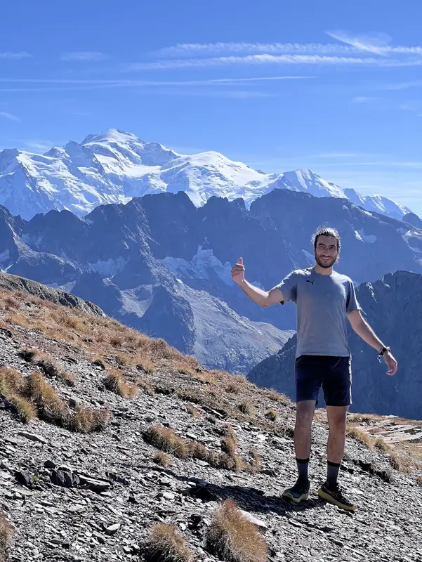 Eine Person auf einem trockenen Grat, im Hintergrund füllt die Schneekuppe des Mont Blanc den Horizont jenseits des Tals.