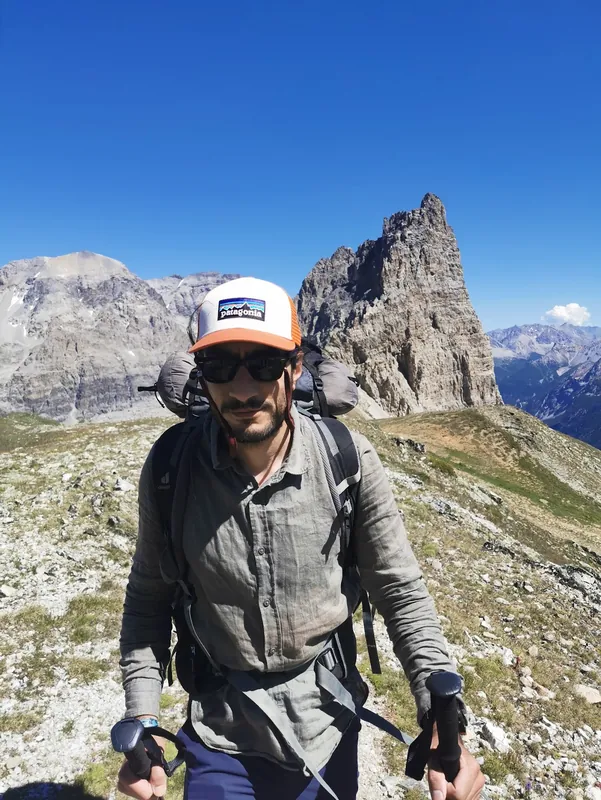 Eine Person mit Kappe und Sonnenbrille auf einer hohen Querung in der Mont-Blanc-Region, dahinter ein steiler Felsturm.