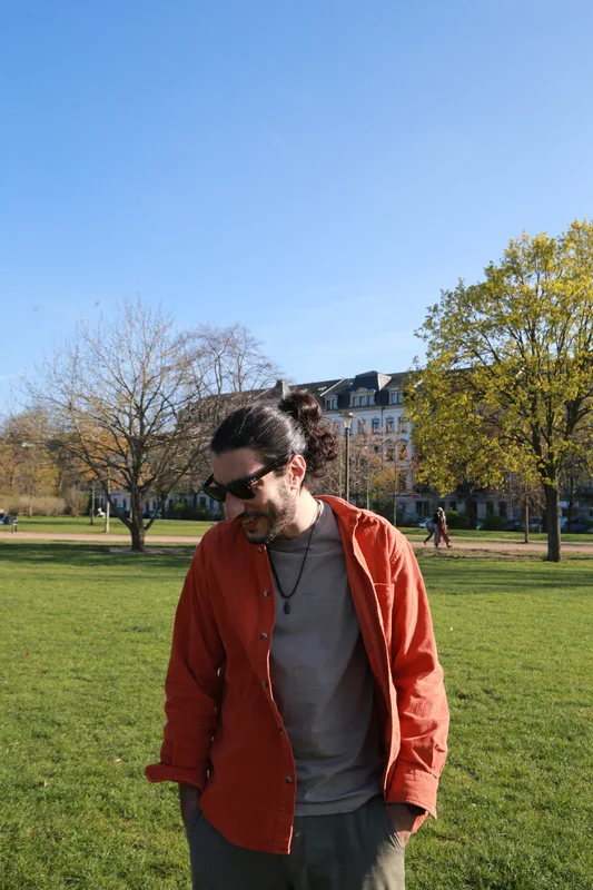 Pejman Shojaee steht an einem hellen Herbstnachmittag in einem Dresdner Park, dahinter gelb werdende Bäume.