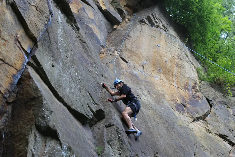 Eine kletternde Person auf halber Höhe einer steilen Sandsteinwand am Seil.