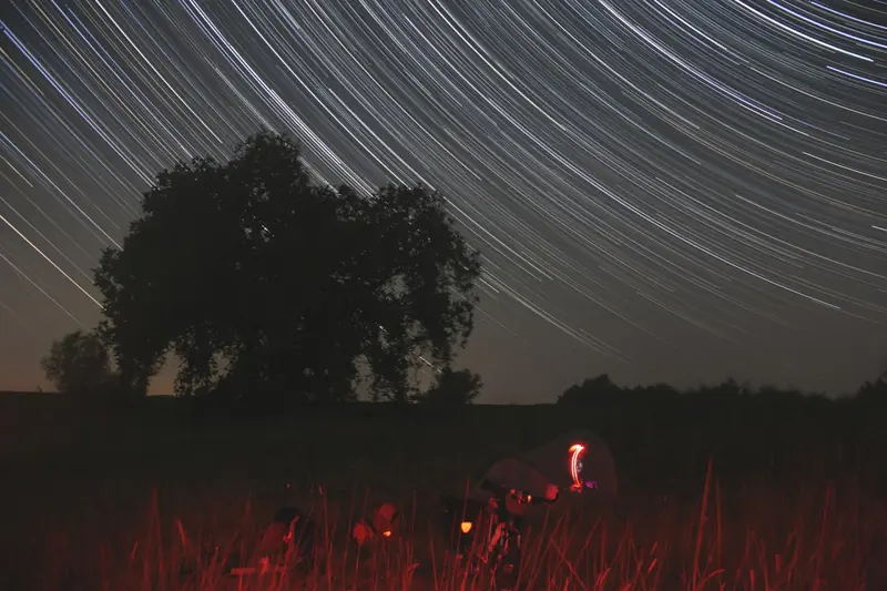 Star trails above an observing site, the gear lit in red to preserve dark adaptation.