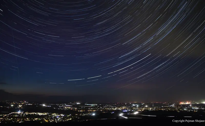 Star trails wheeling over the lights of Zittau, Saxony — a long stack of exposures around the celestial pole.